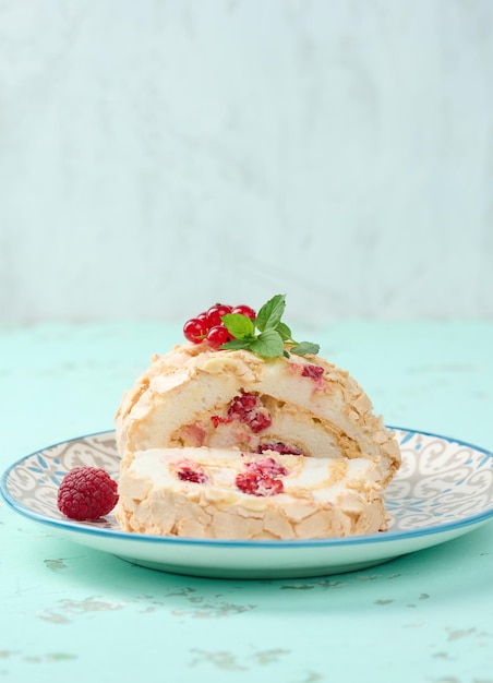 Baked meringue roll with red berries on a round plate white background