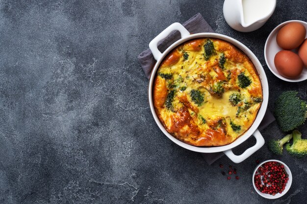 Baked omelet with broccoli in a ceramic dish. Dark concrete table. Copy space. Healthy diet food dish.