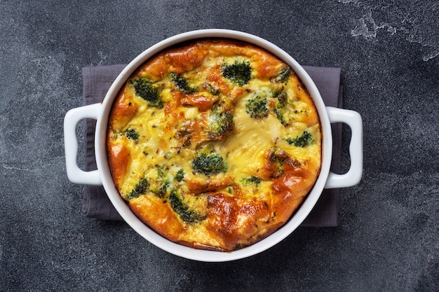 Baked omelet with broccoli in a ceramic dish. Dark concrete table. Copy space. Healthy diet food dish.