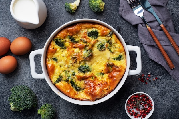 Baked omelet with broccoli in a ceramic dish. Dark concrete table. Healthy diet food dish.