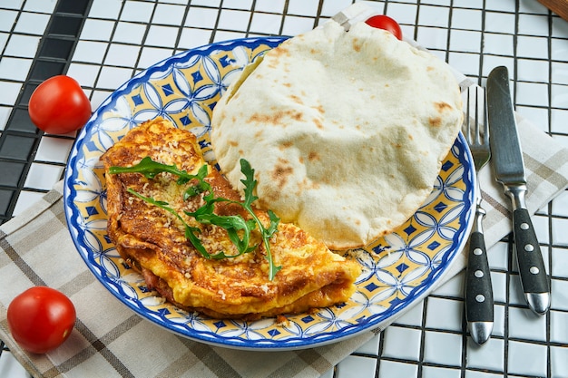 Baked omelet with parmesan and arugula with focaccio bun on an unusual ceramic plate in a composition with ingredients Close up view. Food flat lay