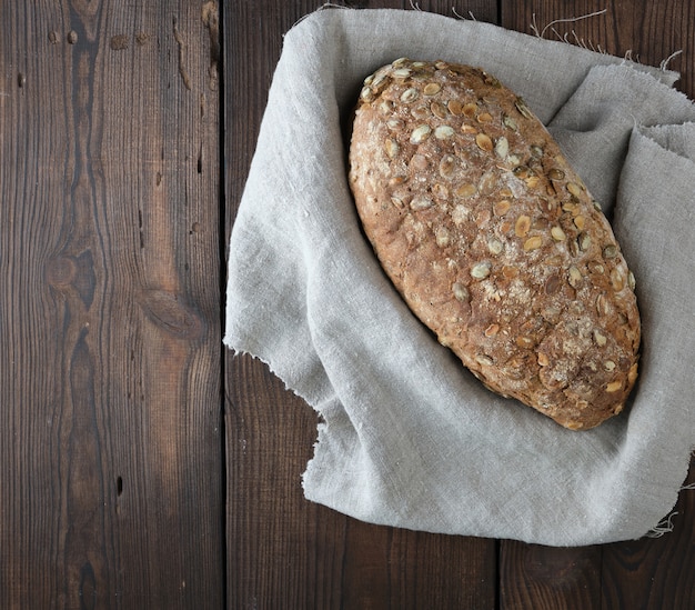 Baked oval bread made from rye flour with pumpkin seeds on a gray linen napkin