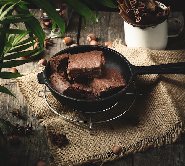 Baked pieces of chocolate brownie cake with walnuts in a black metal frying pan on a wooden table top view