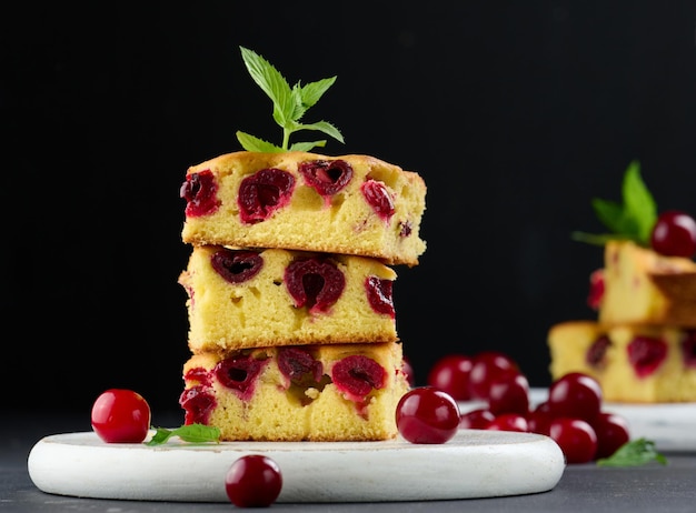 Baked pieces of sponge cake with red ripe cherries on a white wooden board