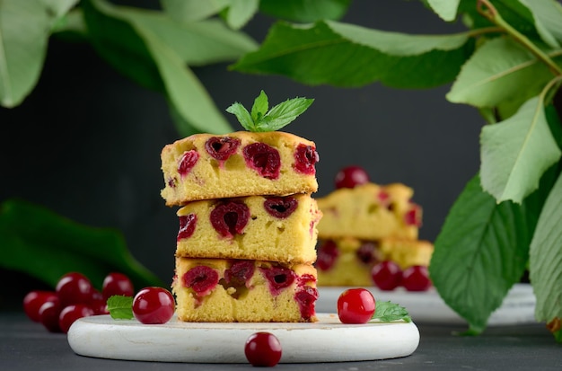 Baked pieces of sponge cake with red ripe cherries on a white wooden board