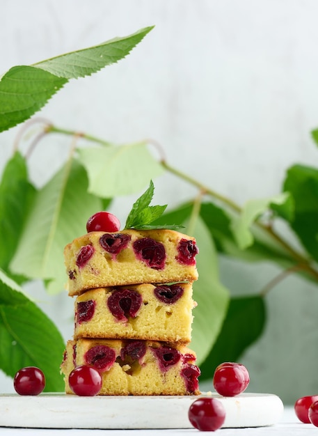 Baked pieces of sponge cake with red ripe cherries on a white wooden board