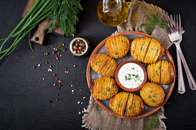 Baked potato with herbs and sauce on black table.