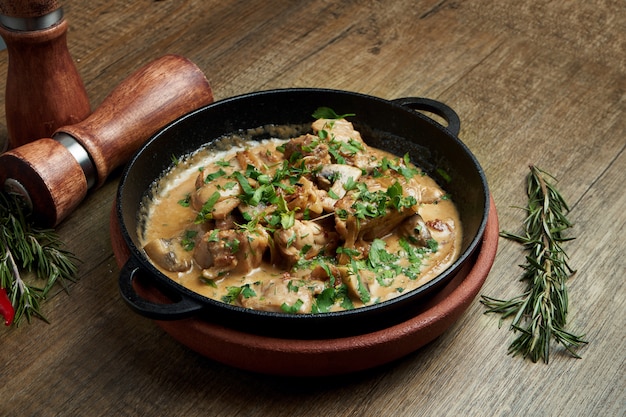 Baked potatoes with chicken in a creamy sauce in a pan on a wooden surface. Close up, selective focus