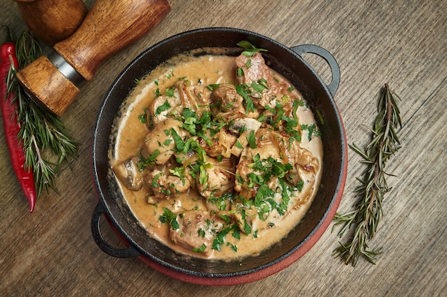 Baked potatoes with chicken in a creamy sauce in a pan on a wooden surface. Top view on tasty food