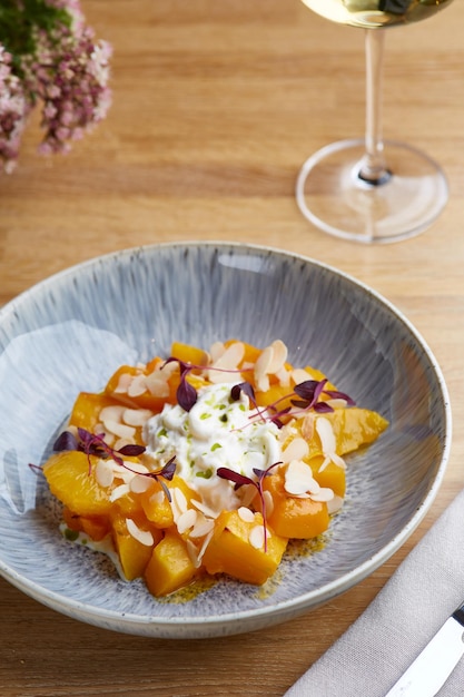 Baked pumpkin in ceramic plate on wooden table with glass of white wine. pumpkin with stracciatella and microgreen