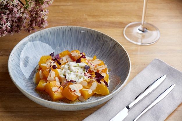 Baked pumpkin in ceramic plate on wooden table with glass of white wine. pumpkin with stracciatella and microgreen.