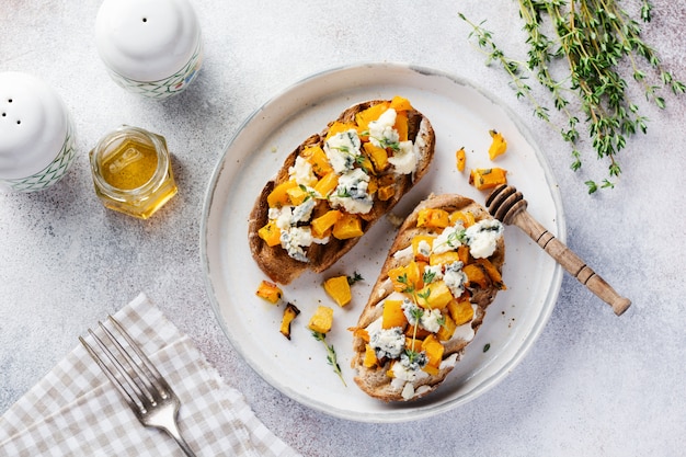 Baked pumpkin sandwich with dorblu cheese with blue mold and thyme on a concrete background