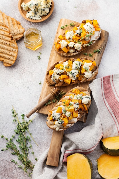 Baked pumpkin sandwich with dorblu cheese with blue mold and thyme on a concrete background