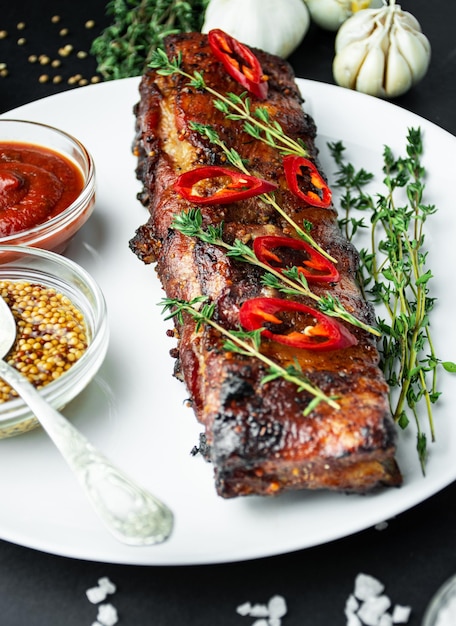 Baked ribs on a plate Roasted ribs with spices and herbs on a dark background Food background Side view Closeup