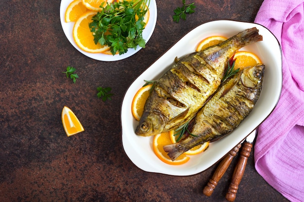 Baked roach fish with vegetables and oranges in a ceramic bowl. Top view. Diet menu.