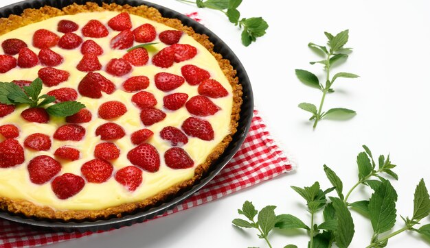 Baked round tart with strawberries and tender milk cream on a white table background, top view