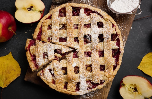 Baked round traditional apple pie on brown wooden board and fresh red apples top view