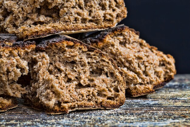 Baked in a rustic oven and then broken into pieces dark bread with a crisp crust on a wooden table