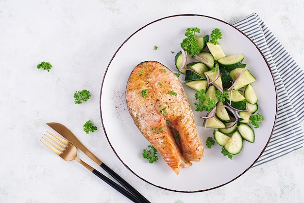 Baked salmon fish steak and fresh cucumber salad with red onions Top view