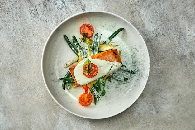 Baked salmon steak with vegetables in a creamy sauce on a plate. Close-up, selective focus.