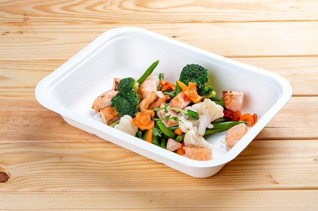 Baked salmon with vegetables Healthy diet Takeaway food Eco packaging On a wooden background