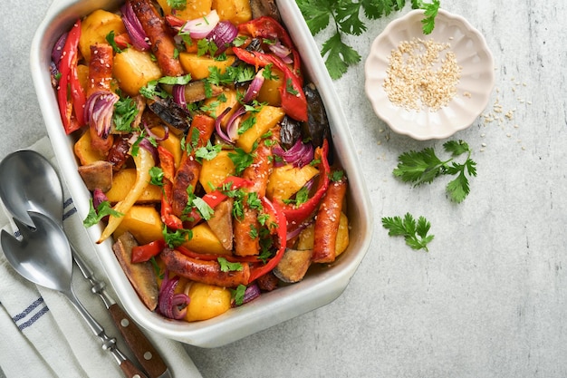 Baked sausage and vegetables peppers zucchini tomatoes red onion and eggplant with sesame and cilantro served hot from oven on baking tray Traditional lunch dish BBQ Sausage jersey tray bake