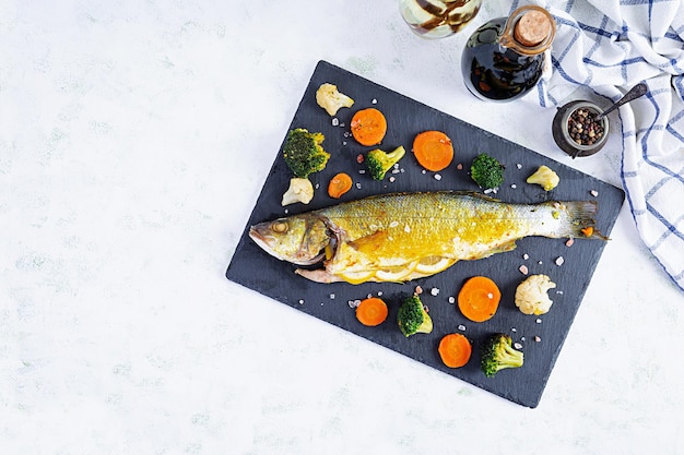 Baked sea bass fish with vegetables and greens on stone plate