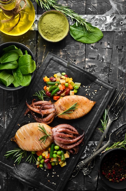 Baked squid with vegetables in a black stone plate Seafood Top view Free space for your text