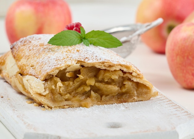 Baked strudel with apples sprinkled with powdered sugar on a white wooden board delicious dessert