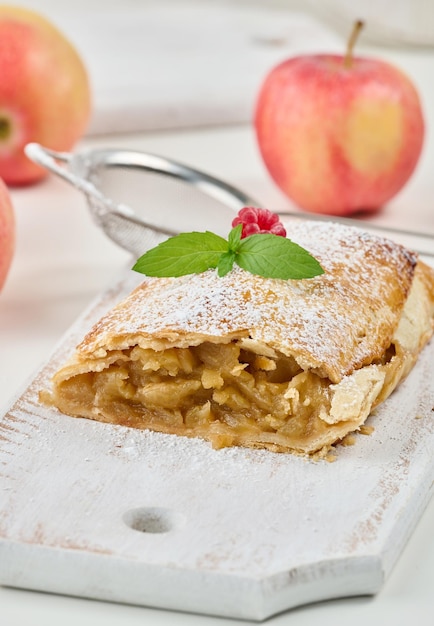 Baked strudel with apples sprinkled with powdered sugar on a white wooden board delicious dessert