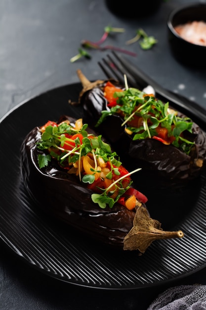 Baked stuffed eggplant with different vegetables, tomato, pepper, onion and parsley on a black stone or concrete table