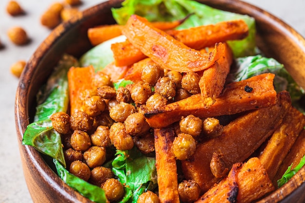 Baked sweet potato wedges and spicy fried chickpea salad in wooden bowl