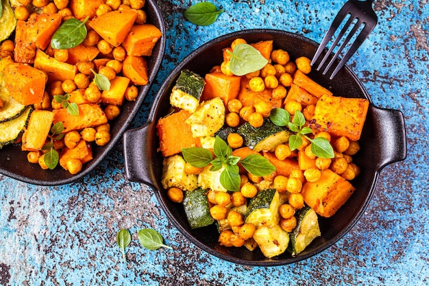 Baked sweet potato zucchini and chickpeas in cast iron pan blue background top view Baked vegetables Healthy food concept