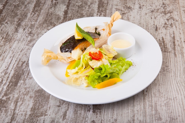 baked trout in paper with salad and white sauce