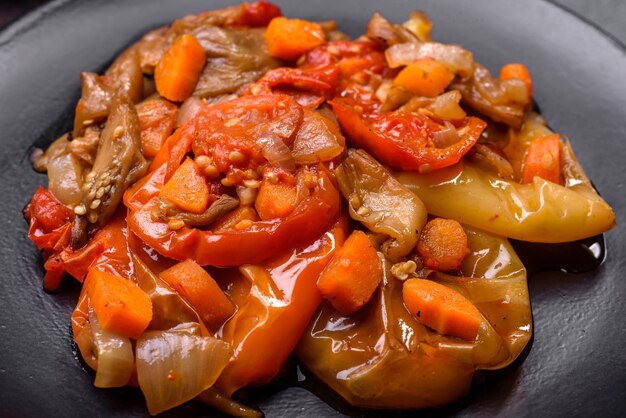 Baked vegetables eggplant peppers and carrots on a black plate on concrete background