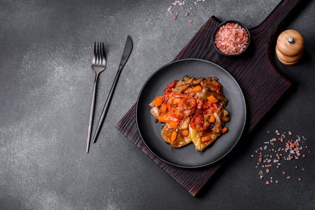 Baked vegetables eggplant peppers and carrots on a black plate on concrete background