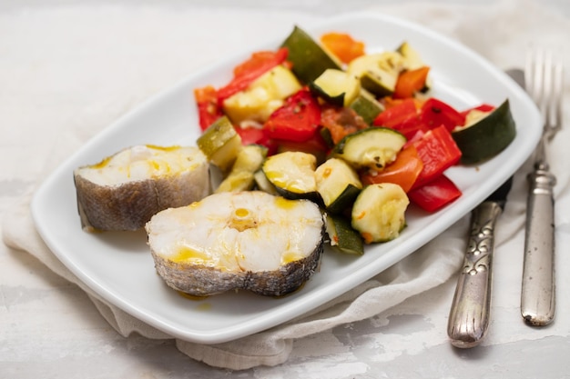 Baked vegetables with boiled fish on white plate