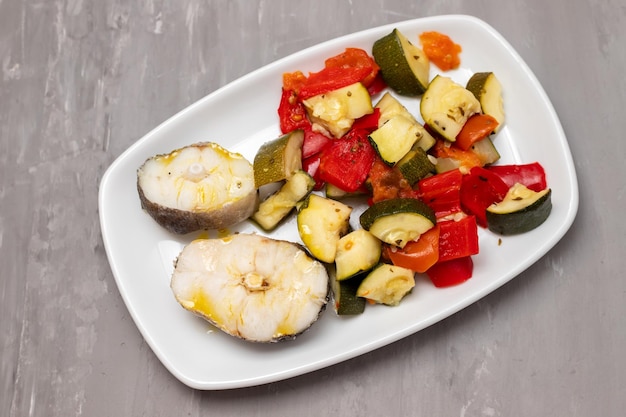 Baked vegetables with boiled fish on white plate