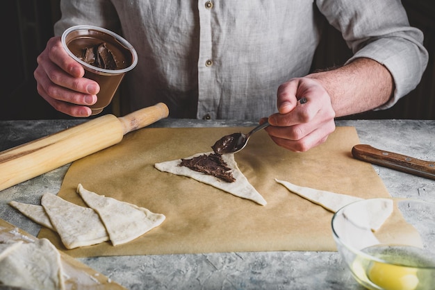 Baker distributes hazelnut spread among puff pastry triangles