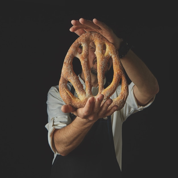 Baker holding fresh organic fougas bread on a dark background