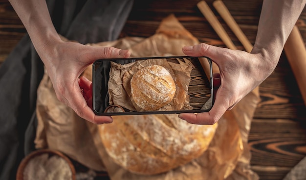 A baker is taking pictures of homemade fresh bread on his phone for a post on social networks Baking bakery products