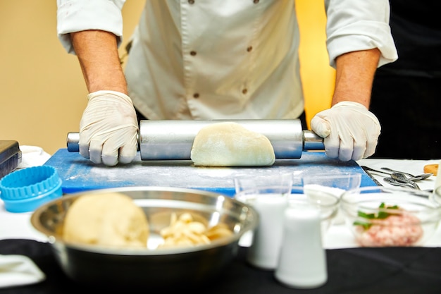 Baker rolls out the dough on a wooden kitchen table sprinkled with flour