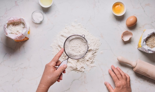 Baker's hand sifting flour by sieve on kitchen counter