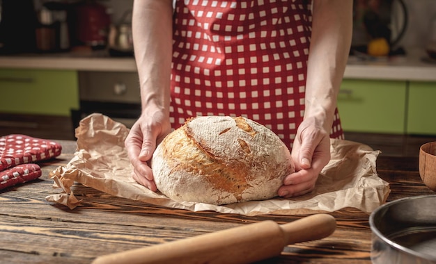 The baker's hands holding homemade natural bread with a Golden crust on a napkin on old wooden background Rustic style