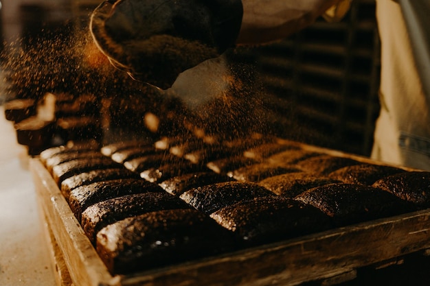 Baker sprinkles flour on the shaped loaves rustic style bread before baking rustic whole grain bread with seeds of sunflower