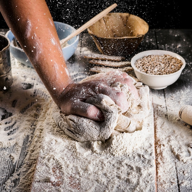 Baker sprinkling the wheat flour on the dough over the kitchen table