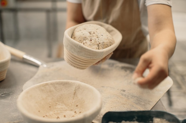 Baker woman sprinkles flour on the shaped loaves rustic style bread before baking rustic whole grain bread