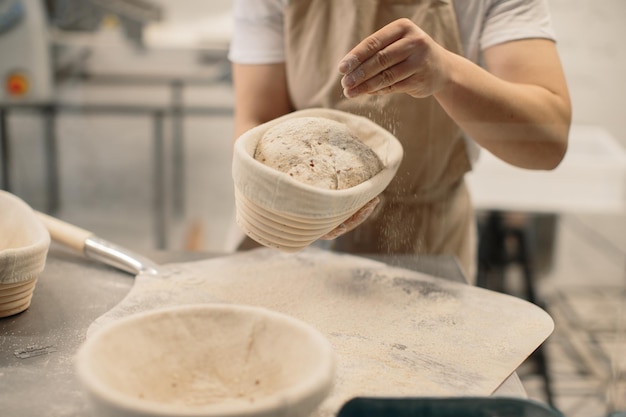 Baker woman sprinkles flour on the shaped loaves rustic style bread before baking rustic whole grain bread