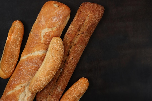 Bakery products on the background of a wooden dark table top view Baguettes sesame buns and long loaf fresh fragrant crispy pastries