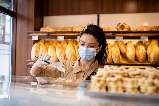 Bakery seller wearing face mask and uniform selling pastry